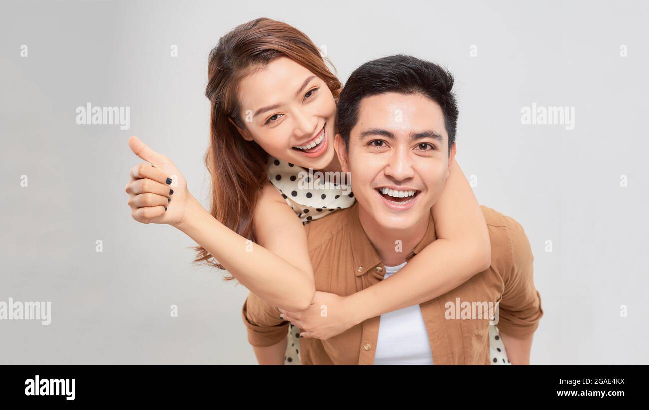 Playful asian happy man piggybacking pretty woman against plain white background Stock Photo