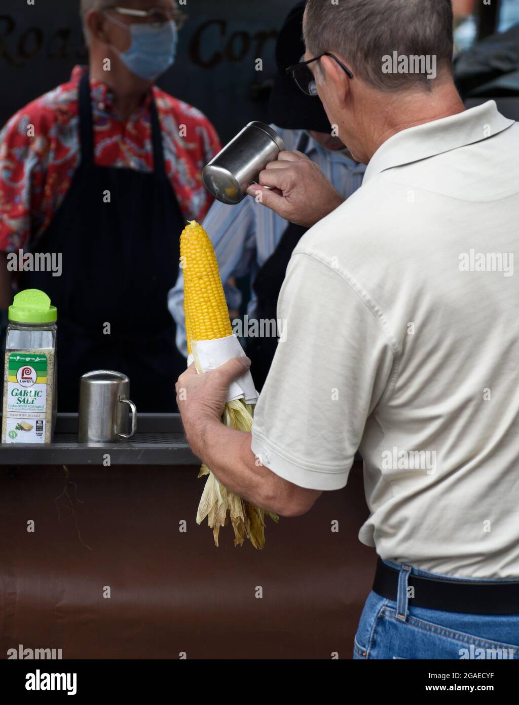 A man buys two ears of roasted corn-on-the-cob from a food stand at an outdoor festival in Santa Fe, New Mexico. Stock Photo