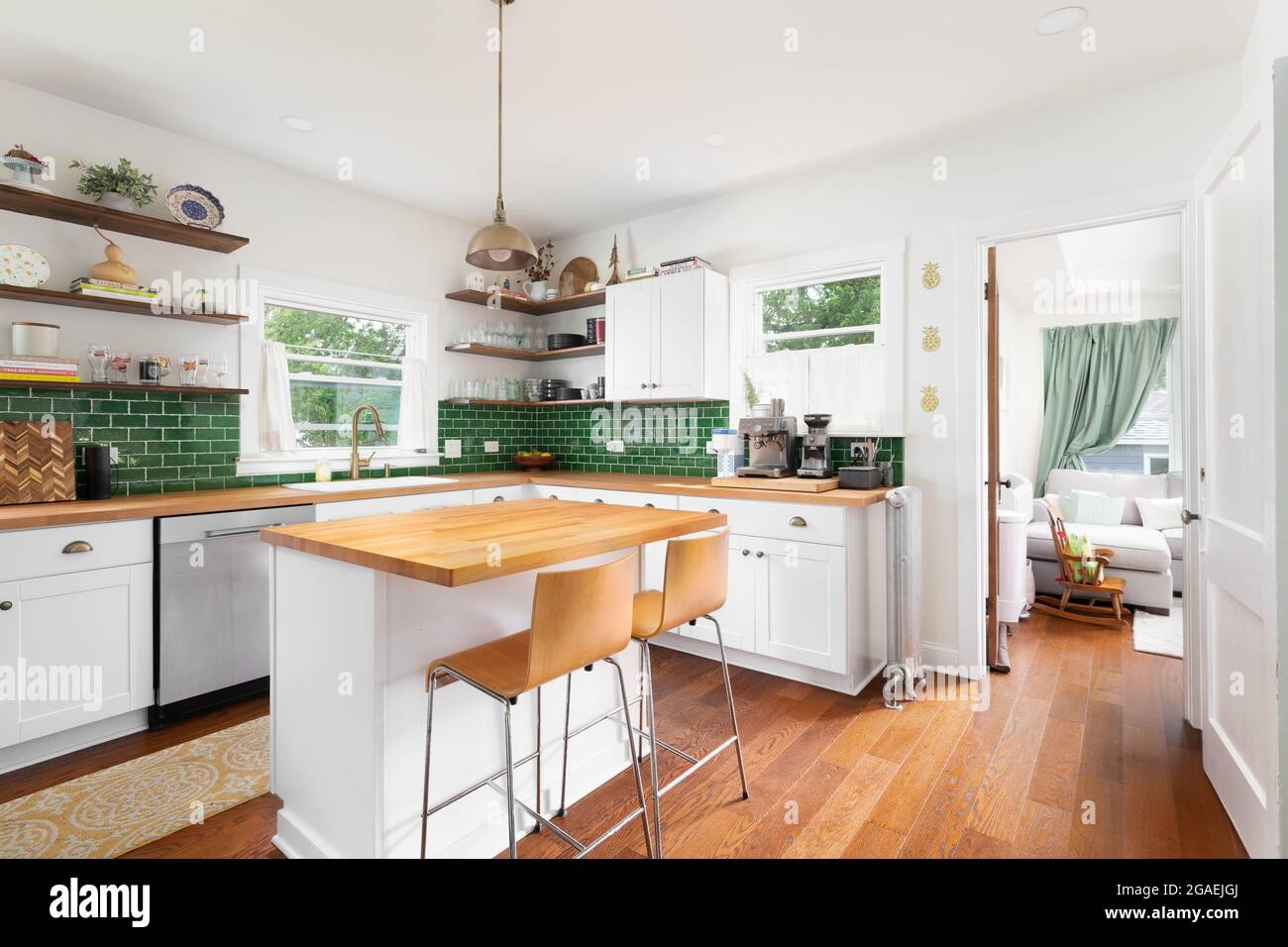 A renovated kitchen with white cabinets, a natural wood countertop, chairs  sitting at the island, and a green subway tile backsplash Stock Photo -  Alamy, image size:1300x956