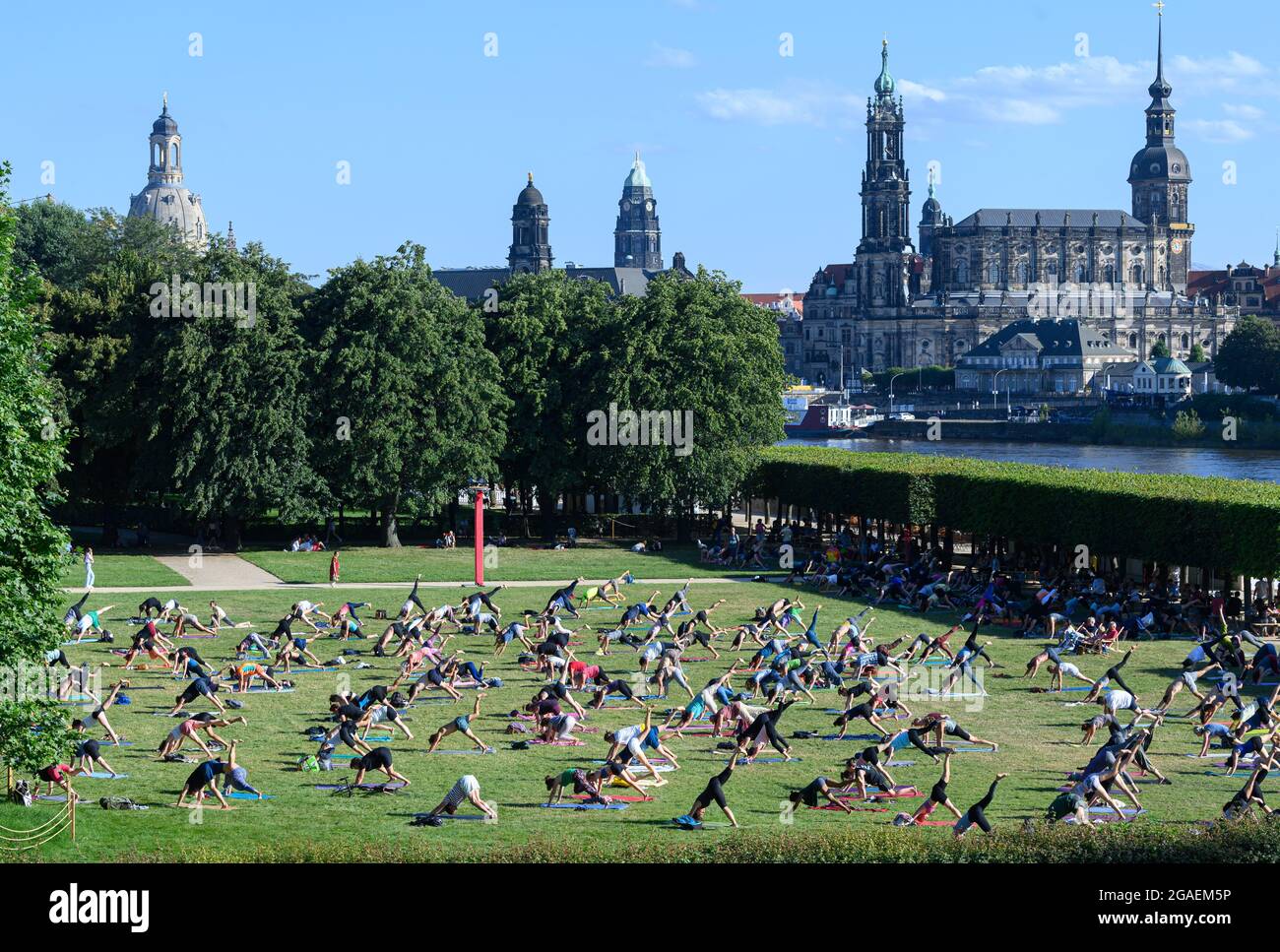 Dresden, Germany. 30th July, 2021. Participants do exercises on a meadow in the evening during a yoga class at the 'Palaissommer' in the Japanese Palace in front of the backdrop of Dresden's Old Town with the Frauenkirche (l-r), the Ständehaus, the City Hall, the Hofkirche and the Hausmannsturm. Credit: Robert Michael/dpa-Zentralbild/dpa/Alamy Live News Stock Photo