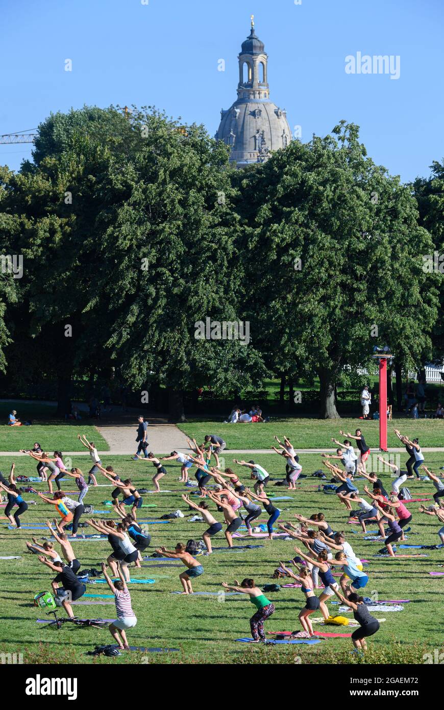 Dresden, Germany. 30th July, 2021. Participants do exercises on a meadow in the evening during a yoga class at the 'Palaissommer' in the Japanese Palais against the backdrop of Dresden's Old Town with the Frauenkirche. Credit: Robert Michael/dpa-Zentralbild/ZB/dpa/Alamy Live News Stock Photo