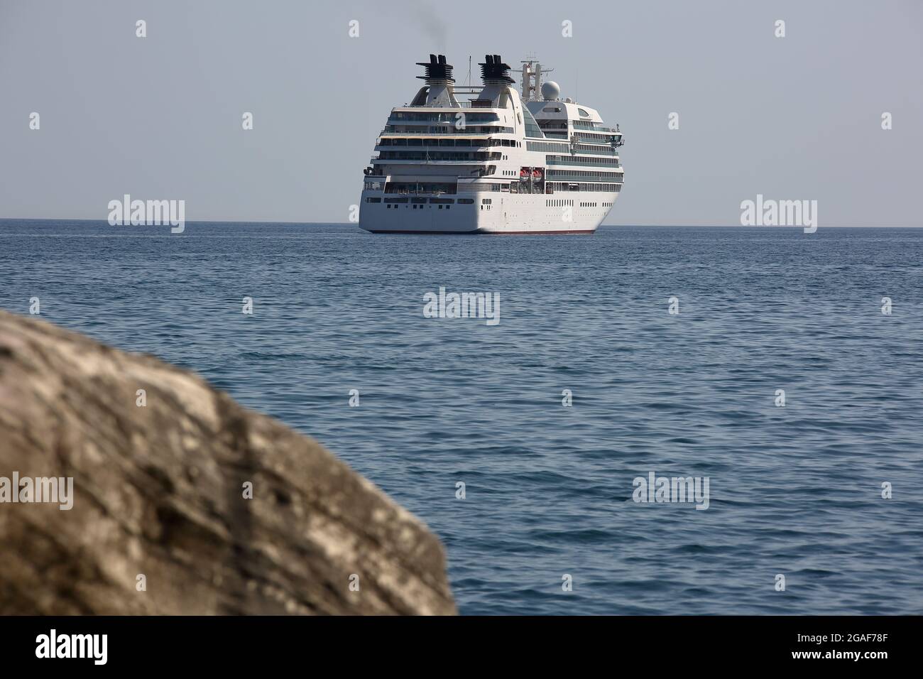 Luxury huge cruise ship on the sea, viewed through coastal white rocks Stock Photo