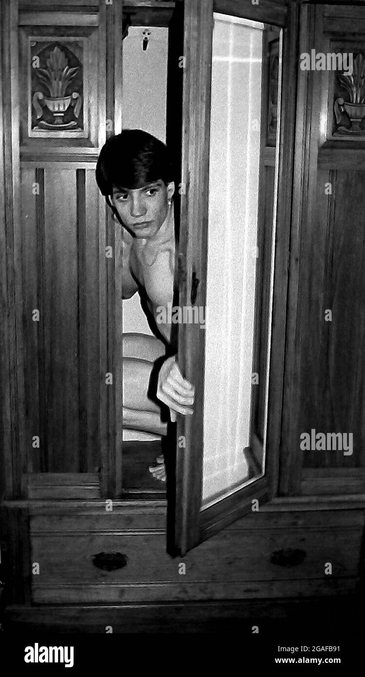 Young gay man comes out is the theme, with an 18 year old man emerging from an old wardrobe or closet. The model was Michael Higginson who later changed his name to Michael Waller. Part of a series taken for Mancunian Gay Magazine in 1984. This image was used for the cover one month. Stock Photo