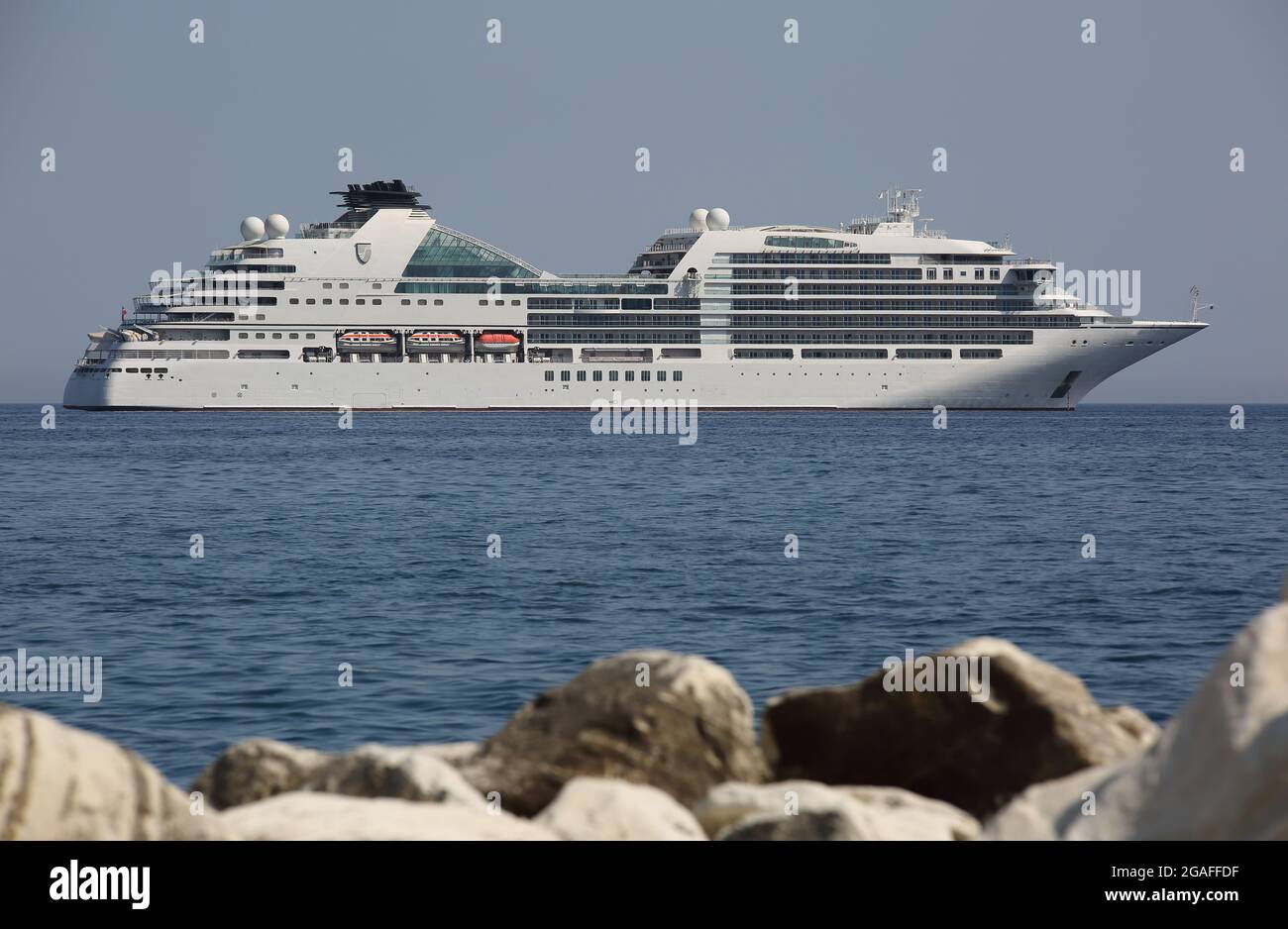 Luxury cruise ship on Mediterranean sea seen from behind rocky beach Stock Photo