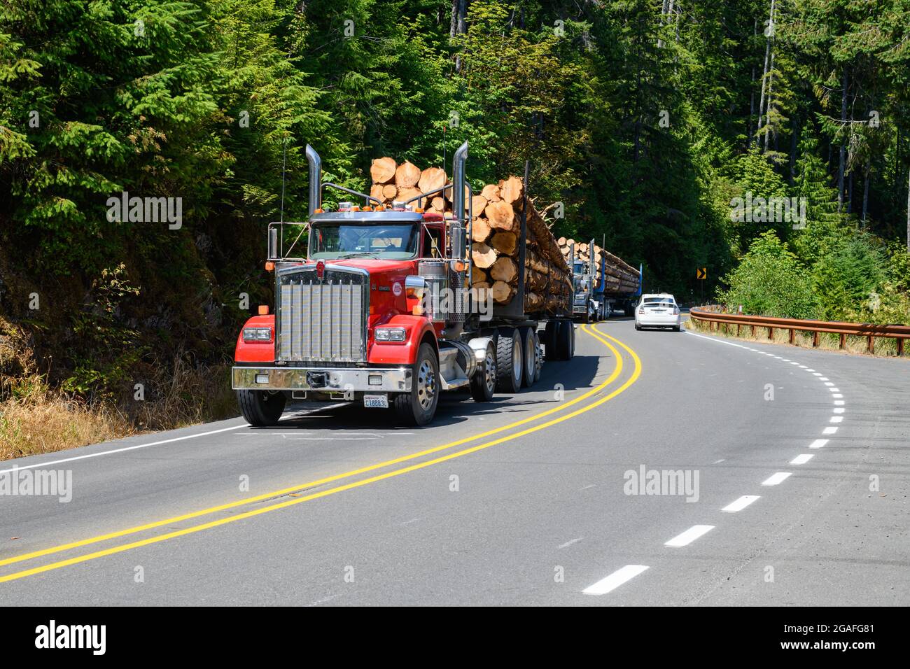 Lake Crescent, WA, USA - July 27, 2021; Loaded logging trucks traveling along the curves of Highway 101 along Lake Crescent in Washington State Stock Photo