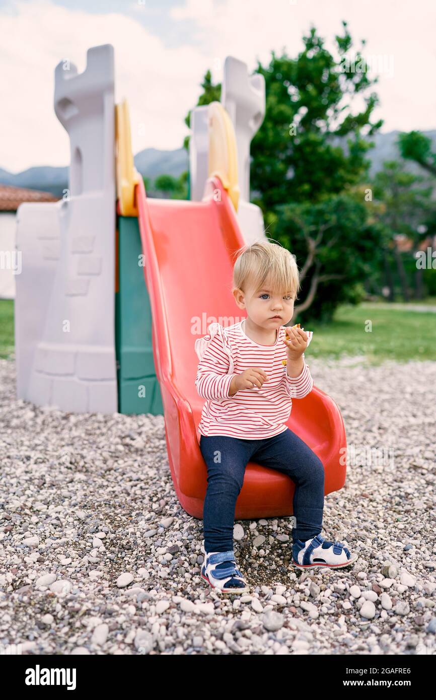 Little girl sitting on a slide in the park Stock Photo - Alamy