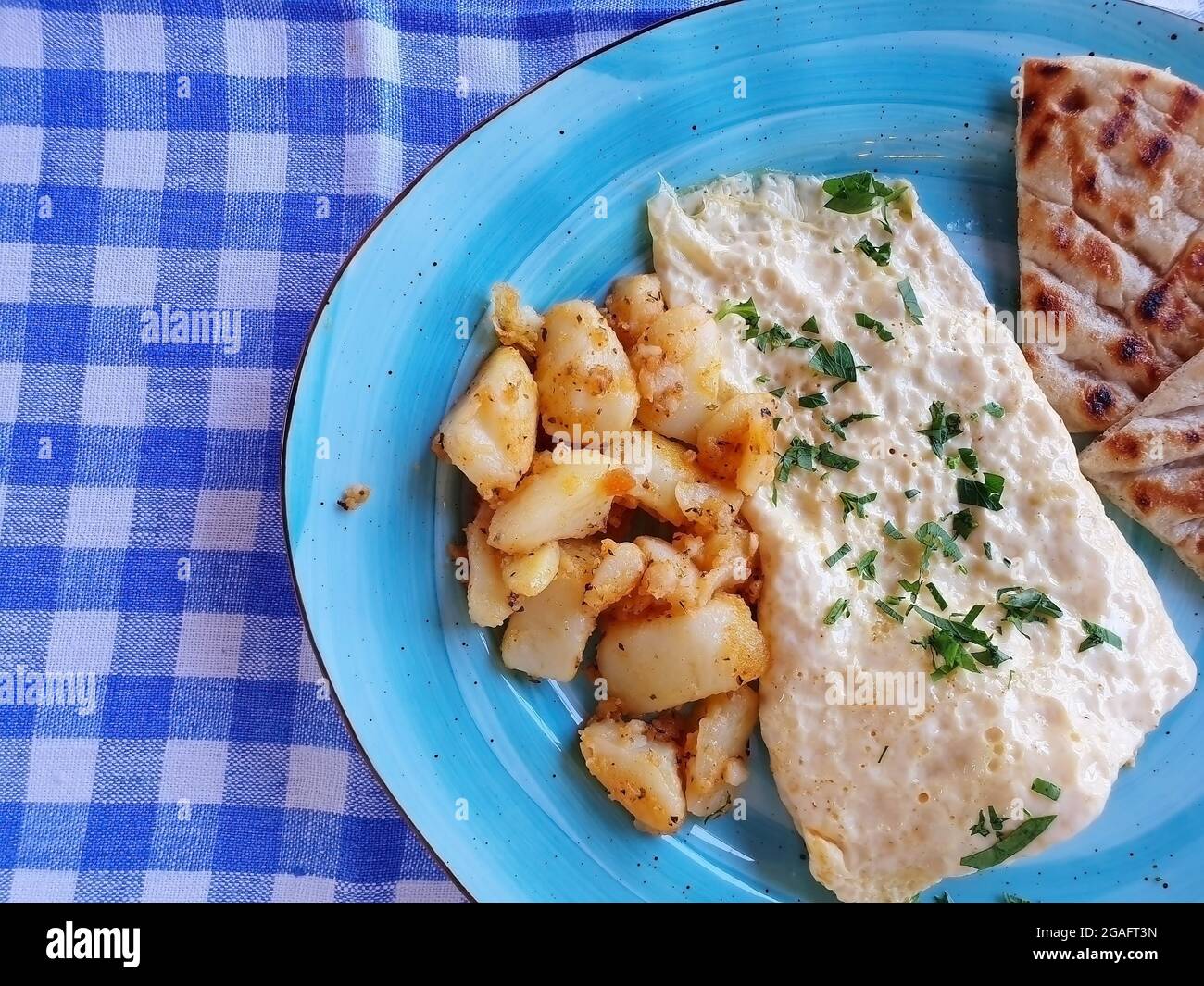 Delicious breakfast of scrambled eggs, potatoes and bread. The food is served on a blue plate. Stock Photo