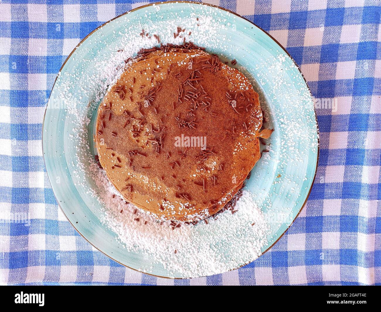 Chocolate pancakes on a blue plate. The pancakes are sprinkled with chocolate chips and powdered sugar. Stock Photo