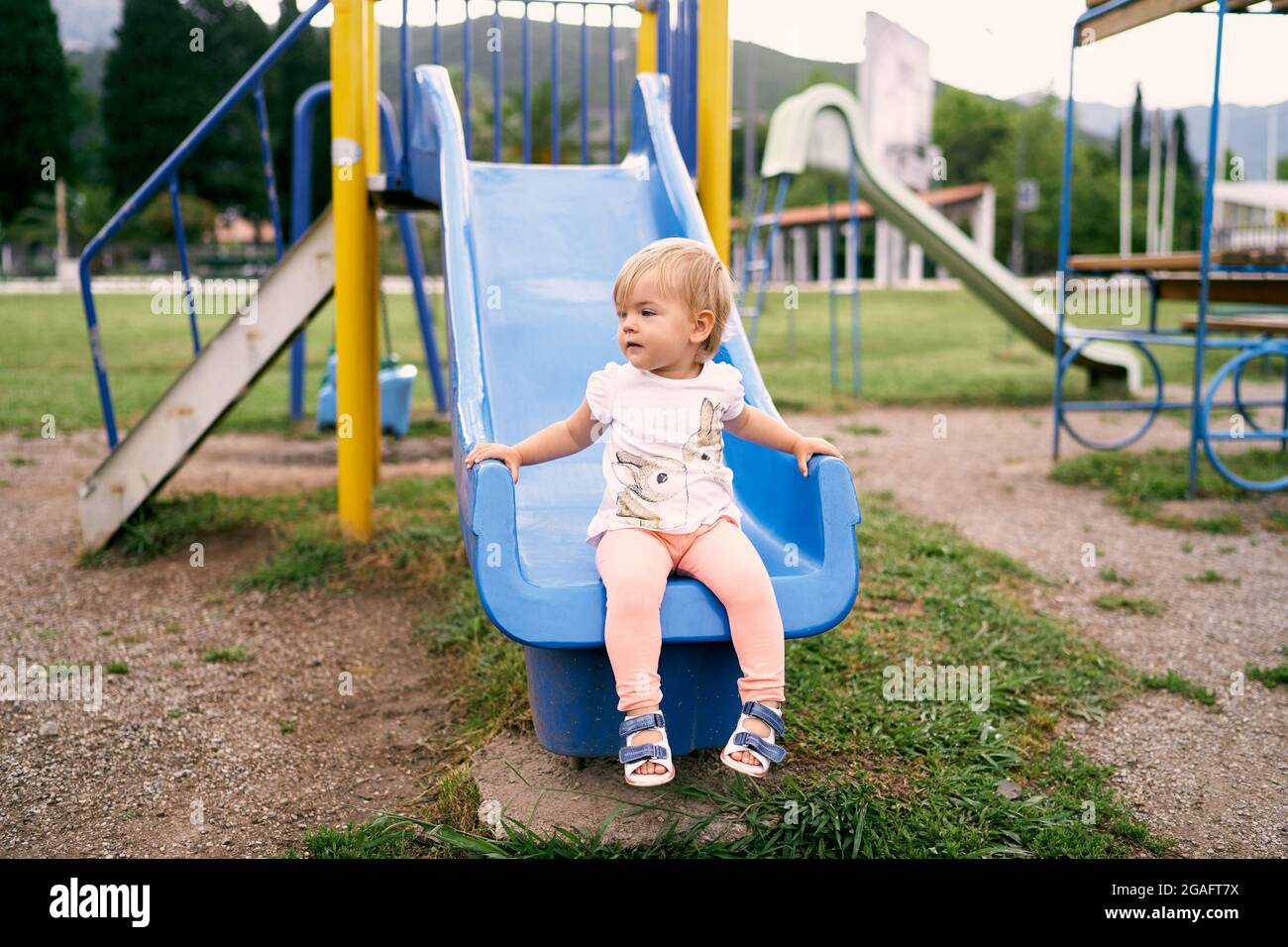 Little girl sits on a slide in the playground and looks away Stock ...