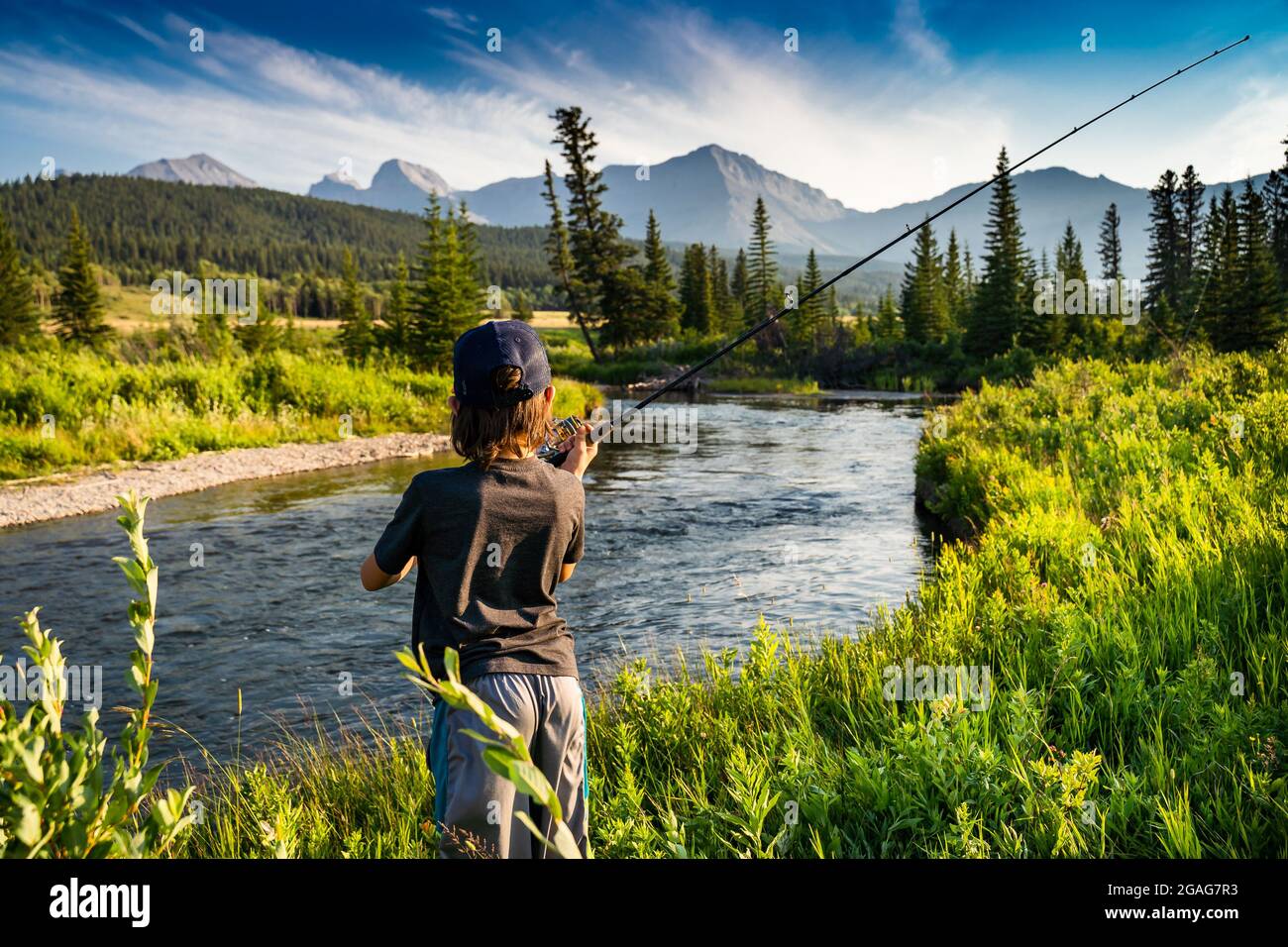A young child casting his fishing rod into the Crossest River with a Rocky mountain backdrop in Southern Alberta Canada. Stock Photo