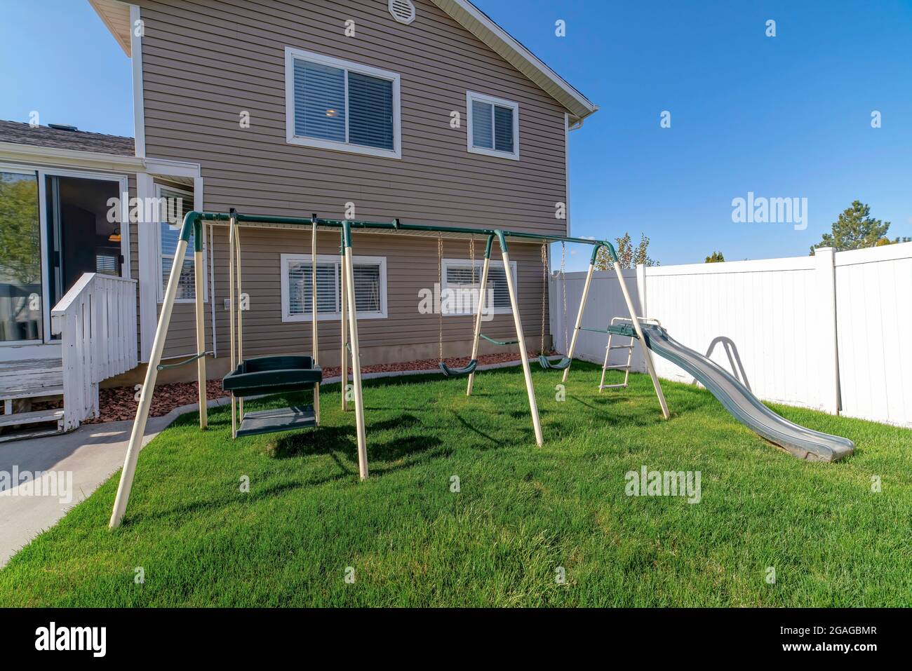 Playground at the lawn of a backyard of a house with white vinyl fence