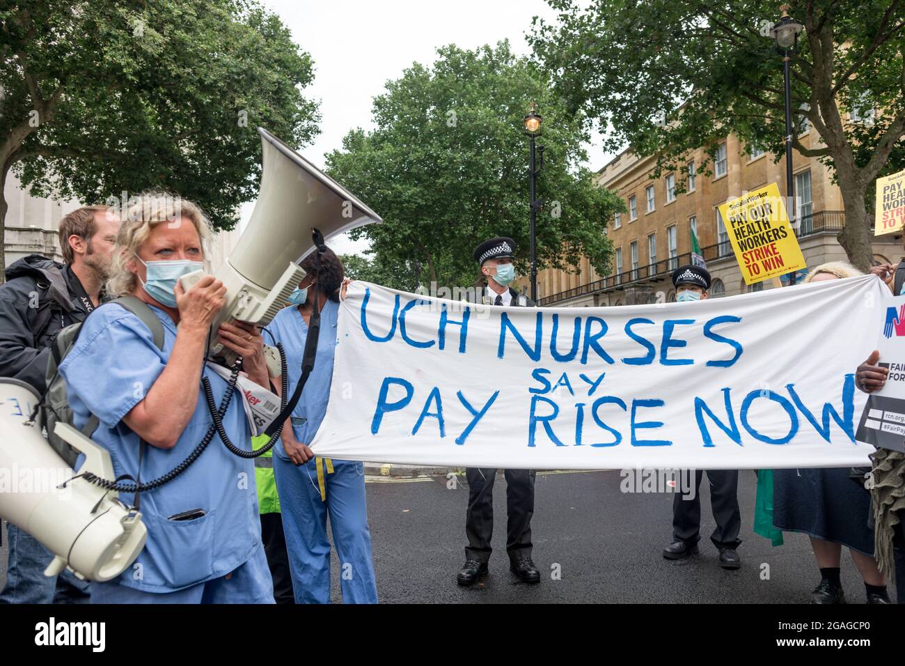 Janet Maiden (L), nurse speaks through a megaphone to other protesters in front of a banner that reads 'UCH Nurses say Pay Rise Now' during a demonstration outside Downing Street.Members of the National Health Service (NHS) gathered outside St. Thomas' Hospital before marching towards Downing Street in a demonstration demanding fair pay for NHS workers, as the government's revised 3% pay rise was deemed hardly satisfactory. Issues addressed included long working hours, understaff and a lack of proper protection materials for the health workers. The demonstration was was led by NHS Workers Say Stock Photo