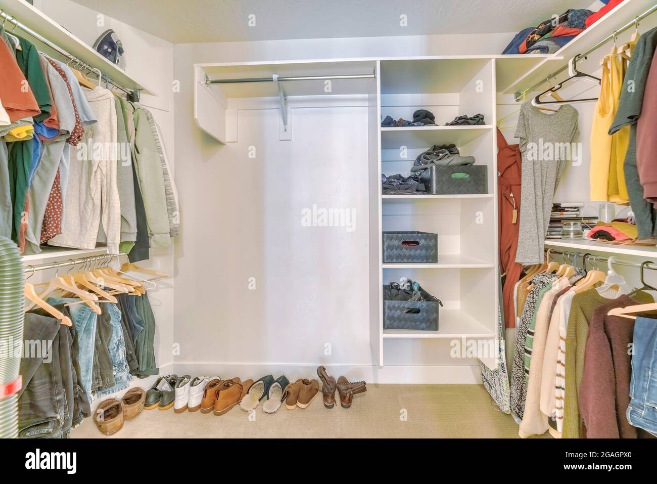 Walk in closet interior with hanging clothes and shoes on the floor Stock Photo