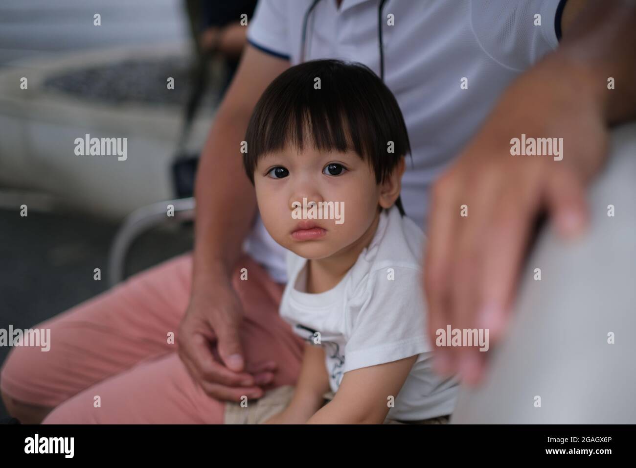 An young Thai boy is looking to camera, while been embraced by father Stock Photo