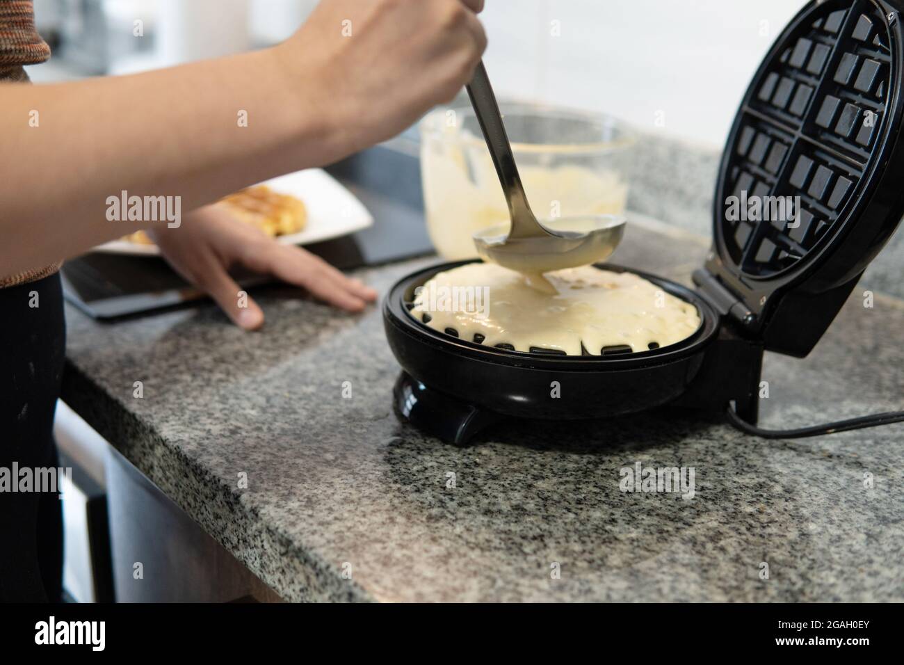 close-up of a hand placing waffle batter in the waffle iron Stock Photo