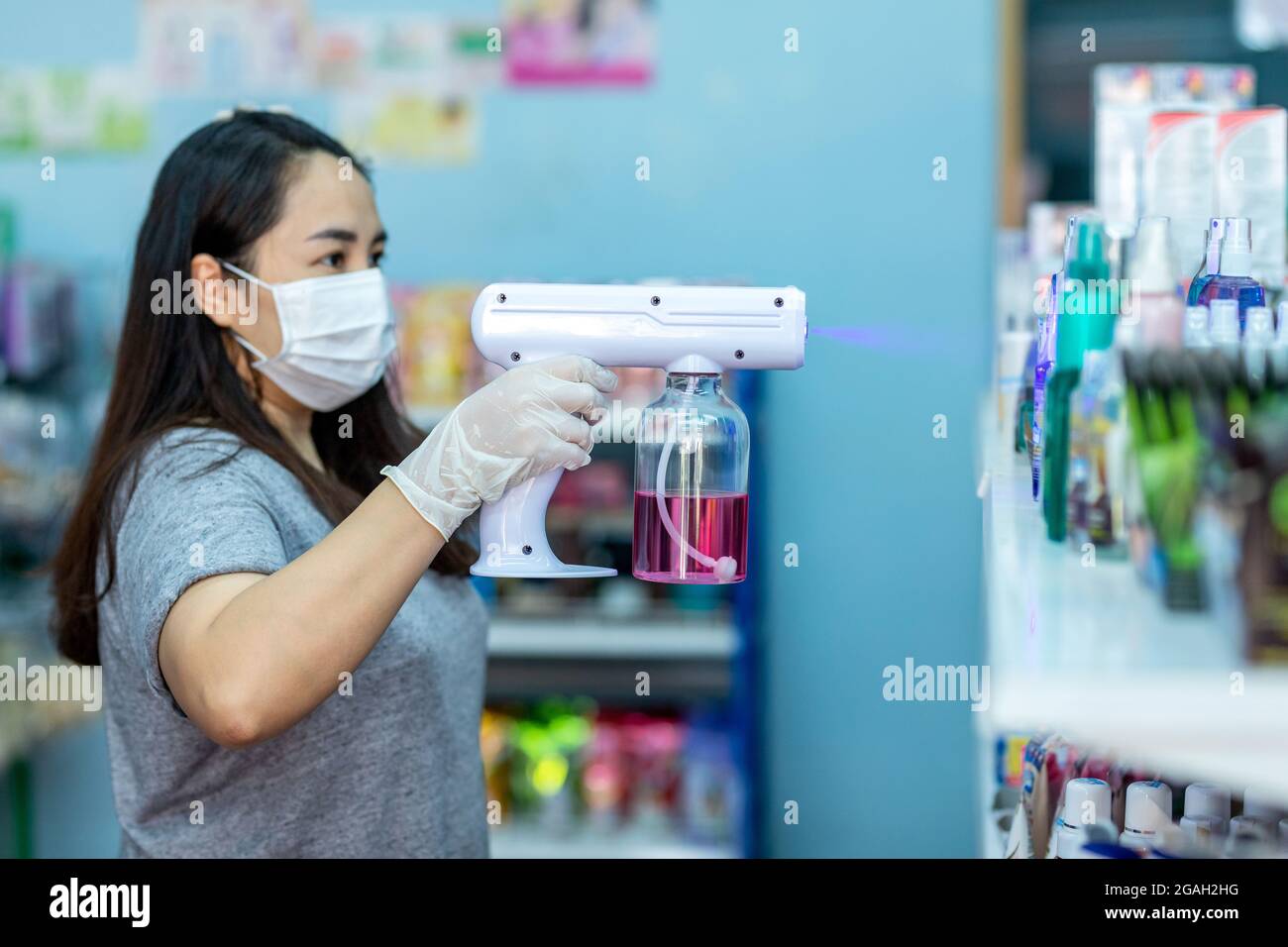 Asian staff wearing gloves using electric Alcohol Nano Spray Gun Handhold Blue Light Disinfectant Spray. prevent infection Covid-19 in the shop. conce Stock Photo