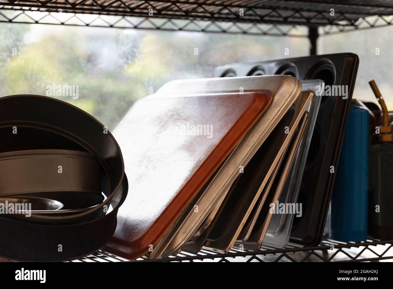 Commercial kitchen baking trays and utensils stacked together on rack. Stock Photo