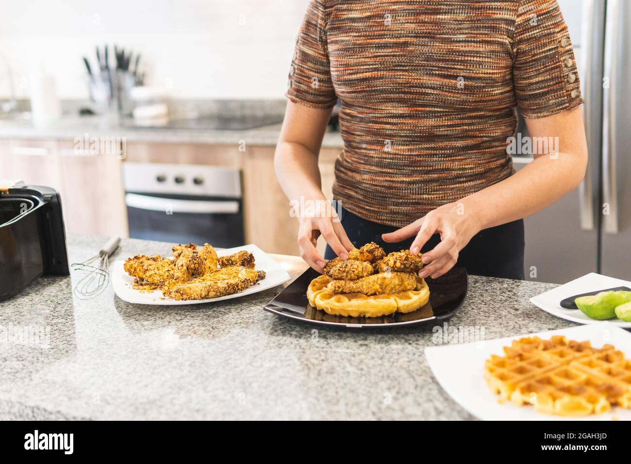 unrecognizable woman plating cereal battered fried chicken over waffles and syrup Stock Photo