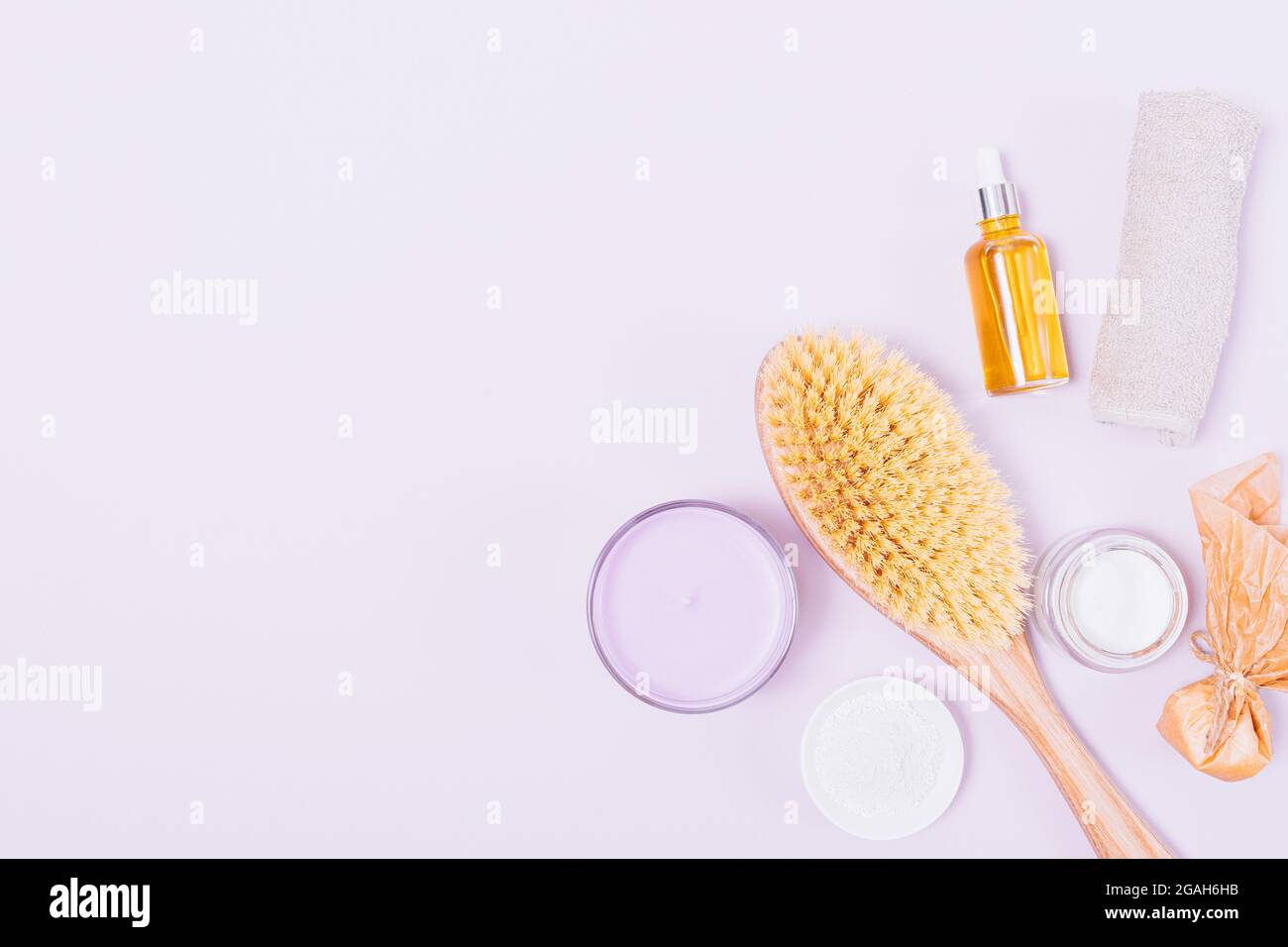 Spa set for home beauty treatments, body massage brush next to cosmetic oils and cream on light purple background with copy space. Stock Photo