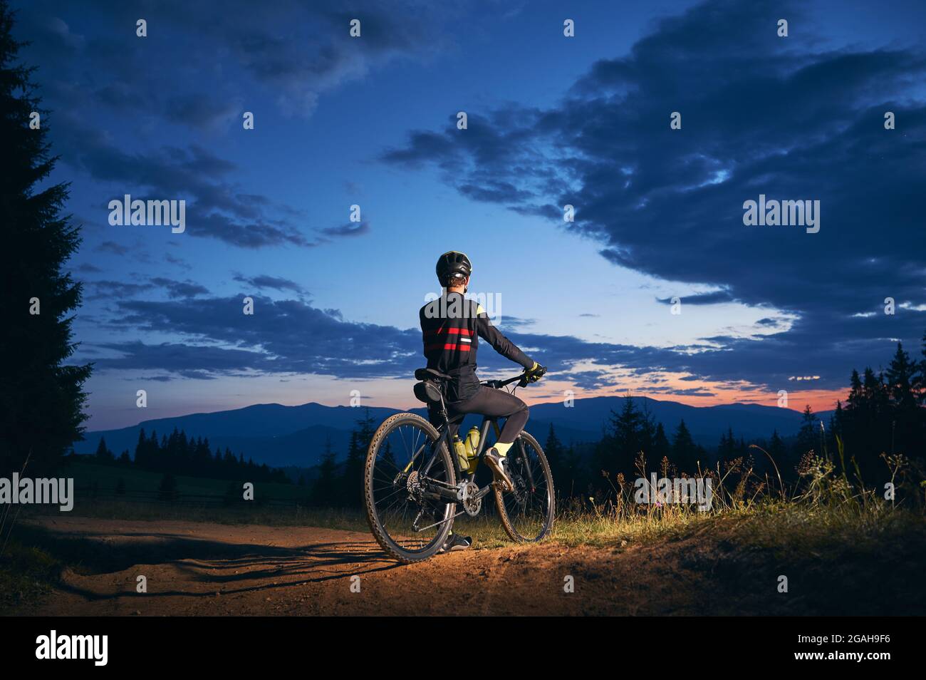Back view of man sitting on bicycle under blue night sky with clouds