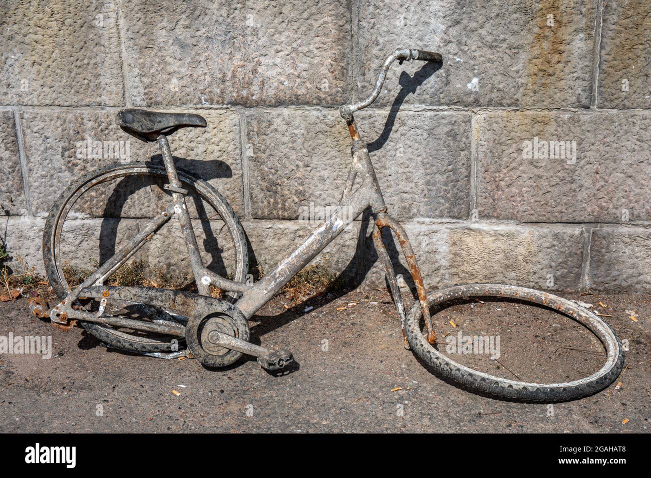 Bicycle wreck salvaged from river leaning against stone wall Stock