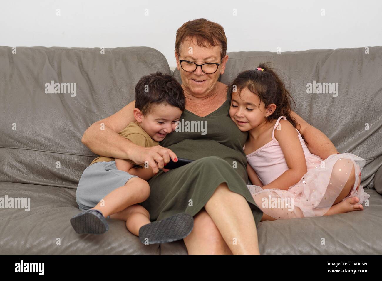 Happy grandma with grandchildren embracing and having fun at home.Senior woman spend time with grandchildren. They are looking online on smartphone together.Reunited family after covid19 pandemic. Stock Photo