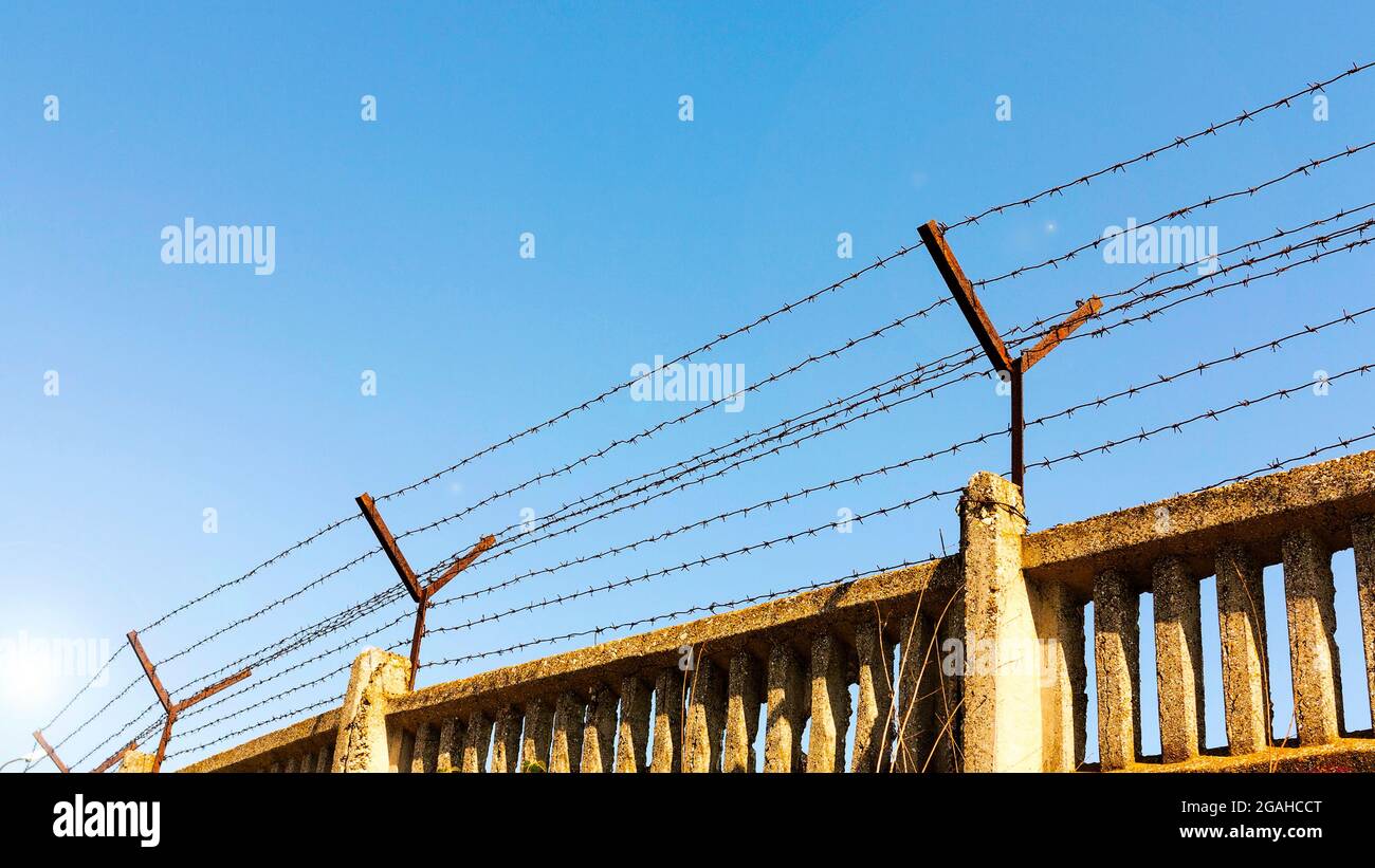 Stone wall with barbed wire against blue sky Stock Photo