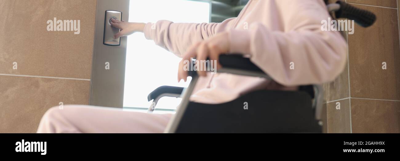 Smiling woman in wheelchair presses button of elevator Stock Photo