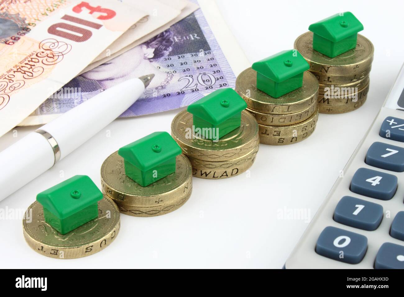 Green houses on rising stacks of coins, to represent eco finance and savings. Stock Photo