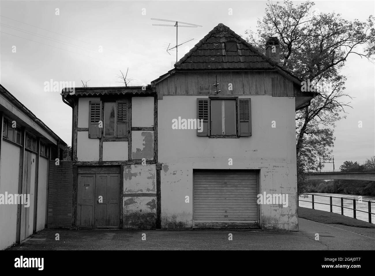 Old abandoned house on the bank of river Aare in Aarburg, Switzerland. There is an analogue aerial on the roof. Photo in black and white. Stock Photo