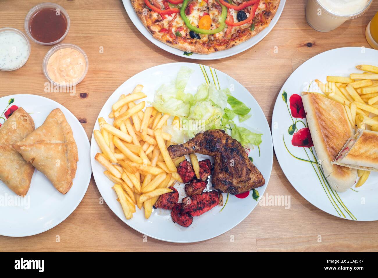 Tandoori chicken with chips and salad, samosas, chicken tikka panini, pizza with dips and drinks Stock Photo