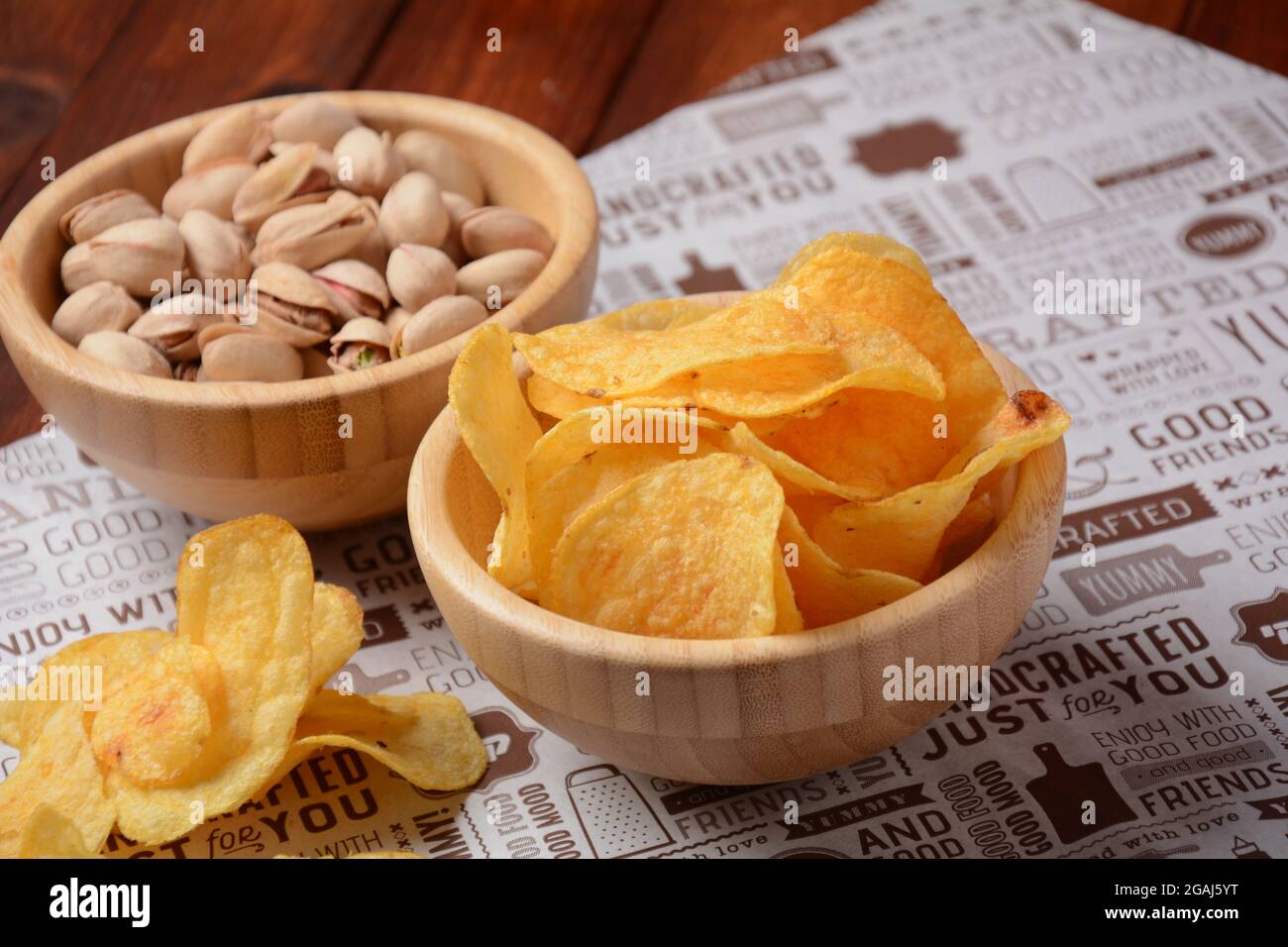 Pistachio nuts, and potato chips in wooden bowls on craft paper. Snacks