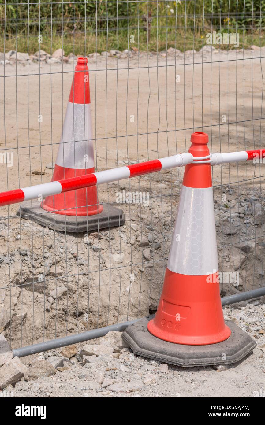 Pair of orange & white warning road cones / safety cones and metal mesh barrier fencing at a construction site. For building site safety, danger area. Stock Photo
