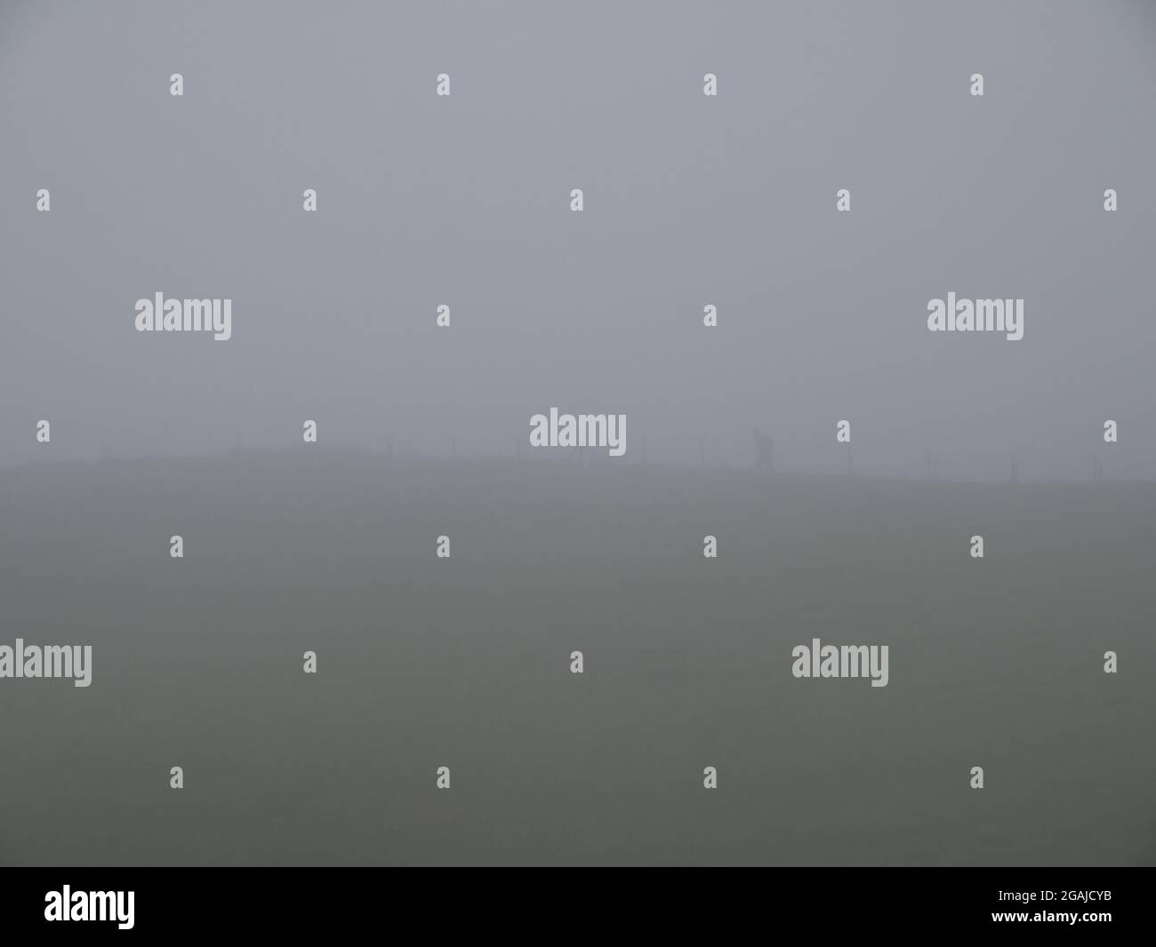 The outline of an unidentifiable single walker on a hill in thick mist and cloud. Stock Photo
