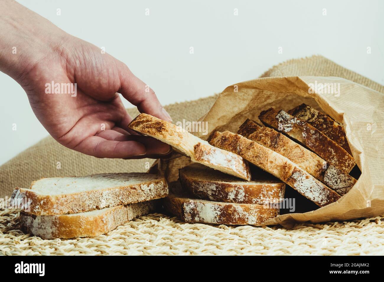 Man's hand picking up a slice of sourdough bread from inside a paper