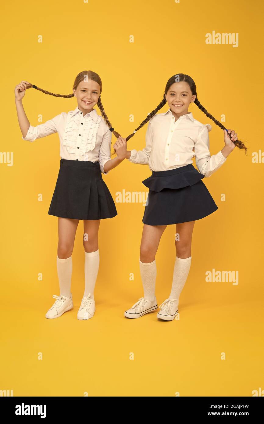 Perfect hairstyle for perfect schoolgirls. Adorable small girls with long hairstyle on yellow background. Cute little children holding braided Stock Photo