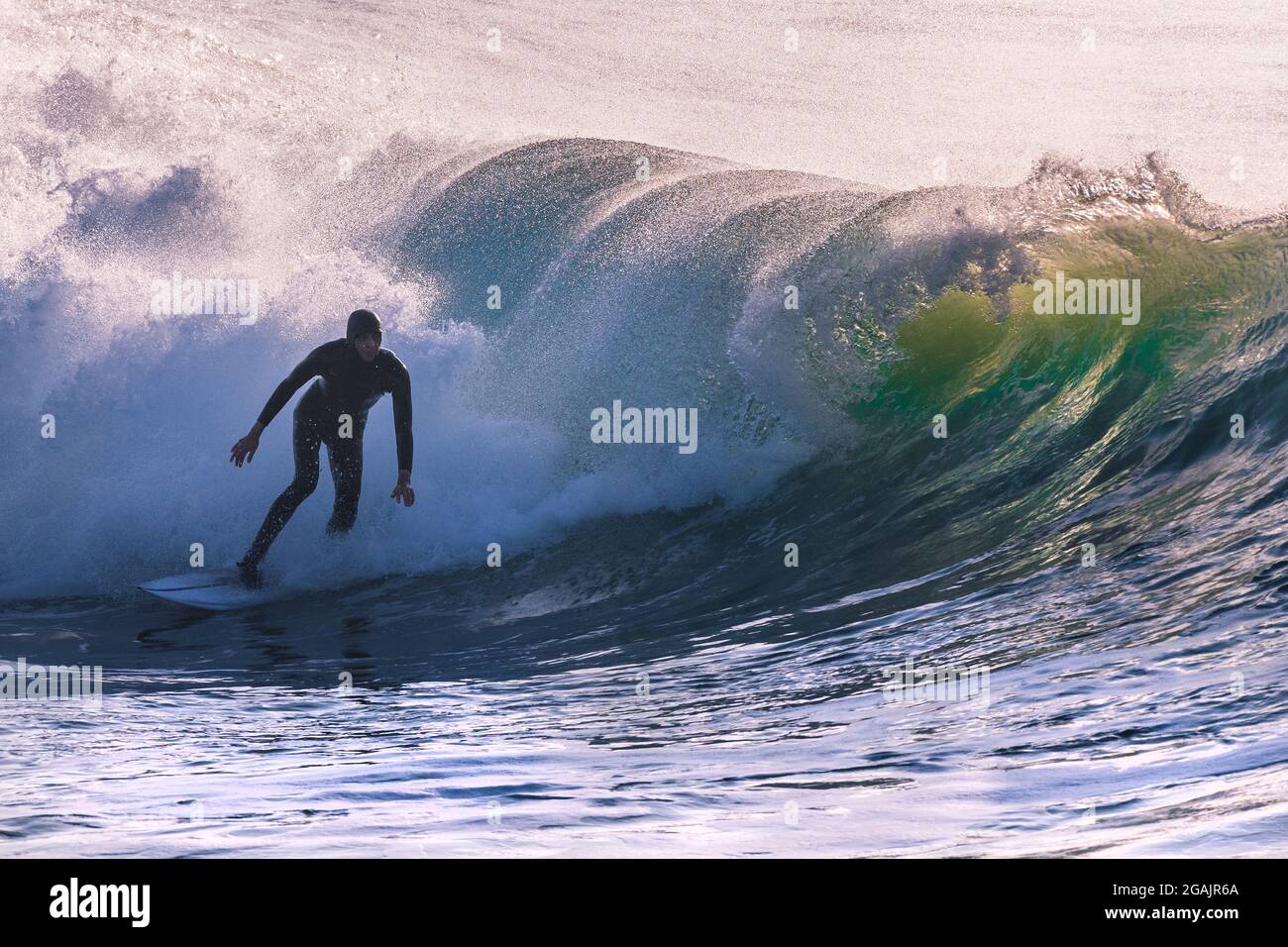 A surfer riding a wave and silhouetted by early evening light at Fistral in Newquay in Cornwall. Stock Photo