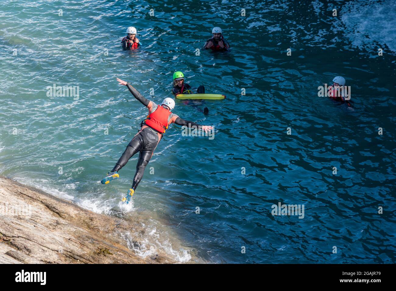 Holidaymakers jumping into the sea with their coasteering guide on the coast of Towan Head in Newquay in Cornwall. Stock Photo