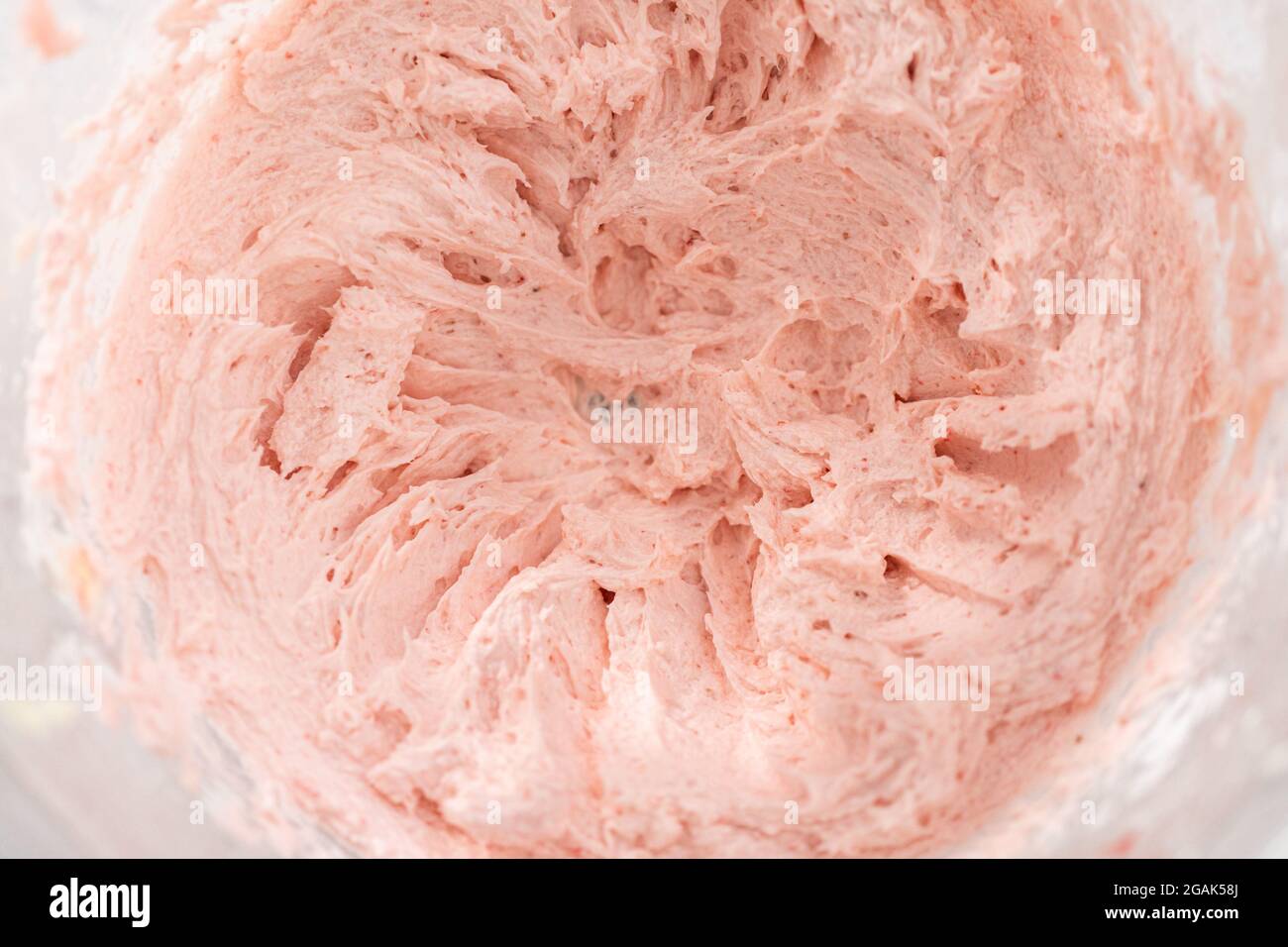 Whipping strawberry buttercream frosting in a standalone electric mixer with a whisk attachment