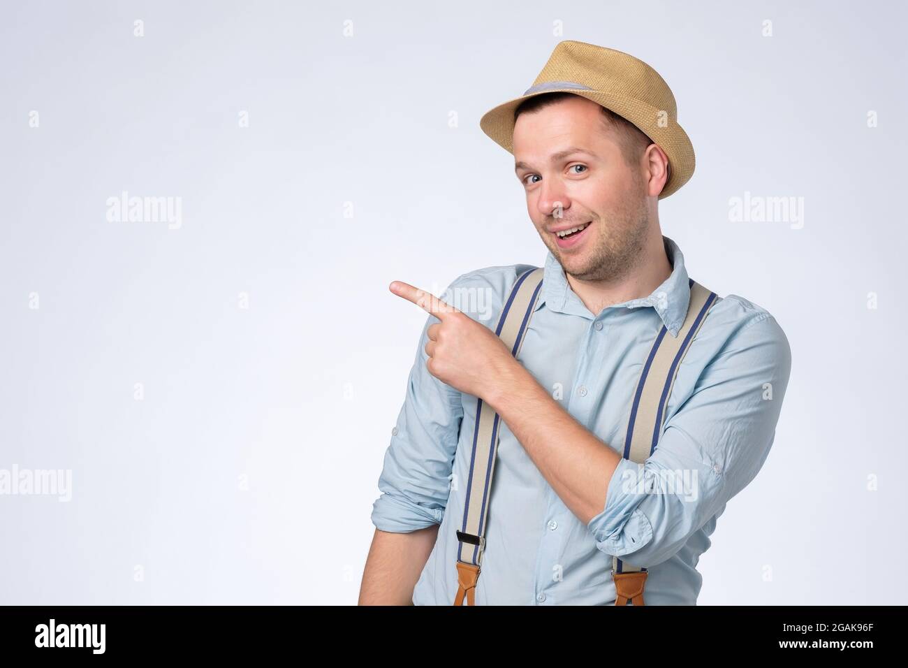 Happy young man in hat pointing aside with forefinger on copyspace. Stock Photo