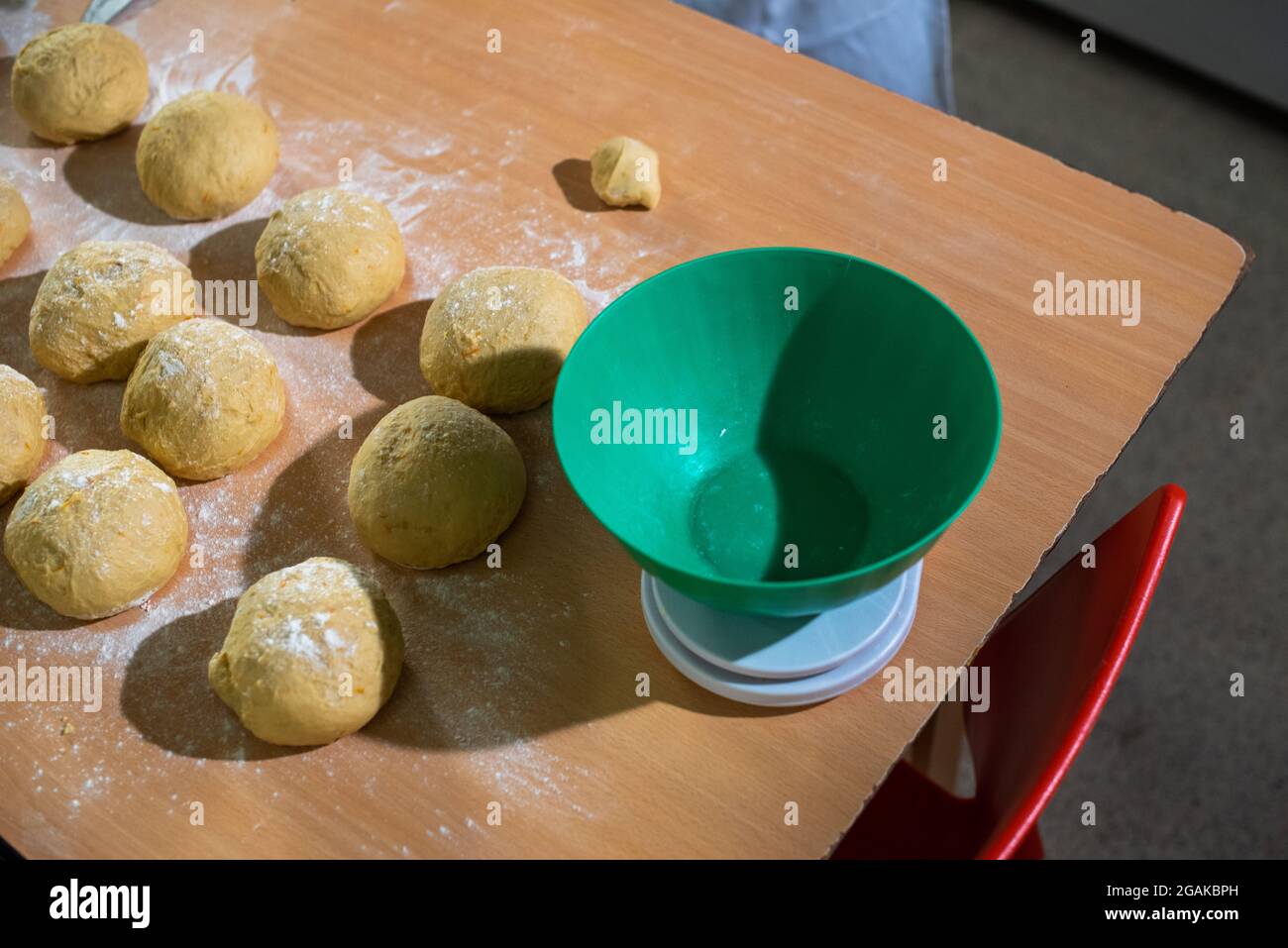 Mujer caucásica masando masa para hacer pan y bizcochos en una mesa color madera con luz de día, en una panadería. Stock Photo