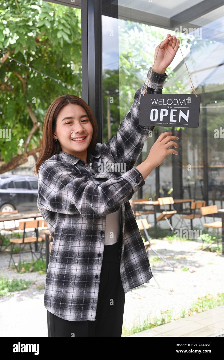 Friendly waitress woman hanging open sign on the glass door. Stock Photo