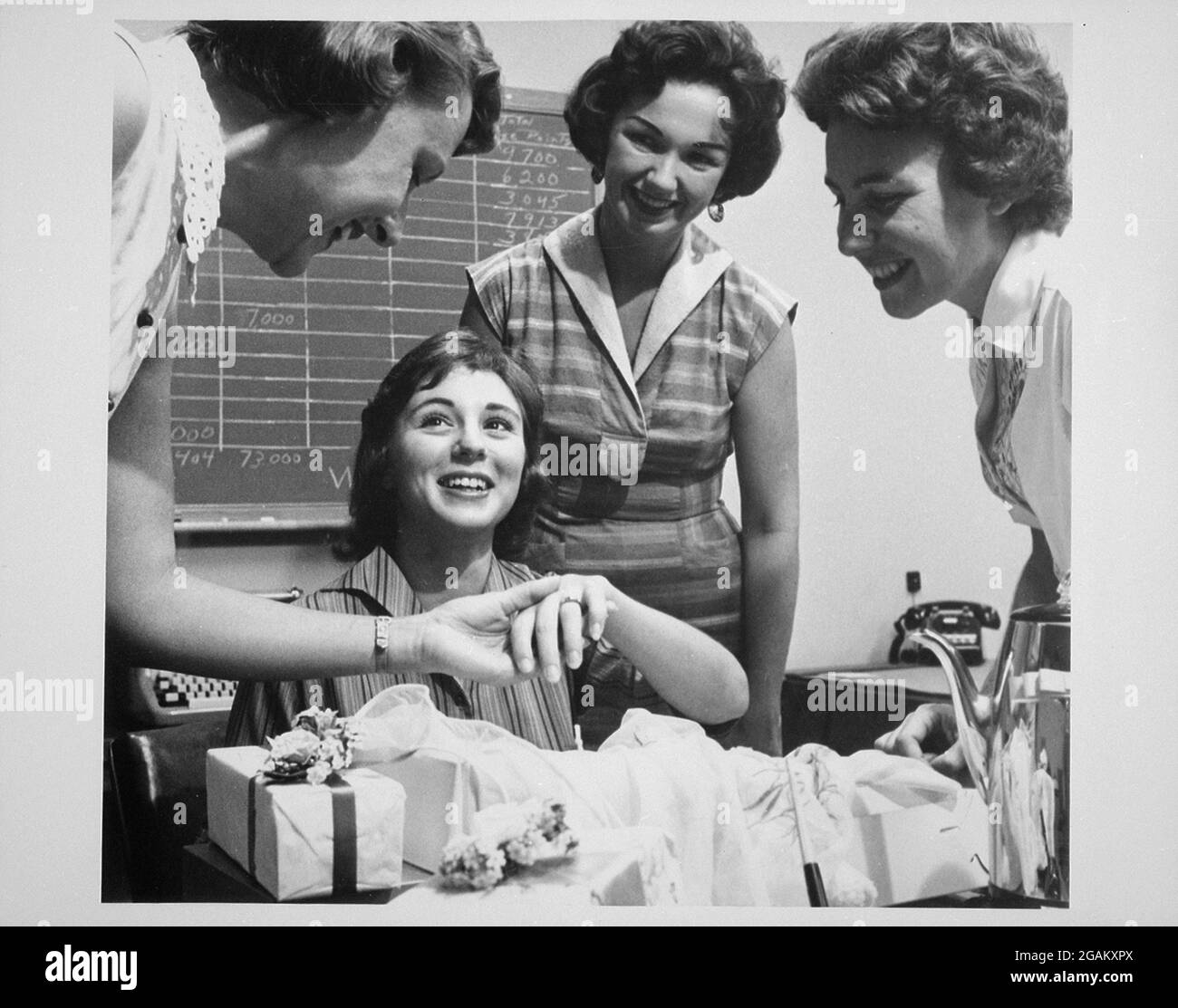 Female co-workers crowd around a beaming bride-to-be as she shows off her engagement ring and receives gifts and congratulations, no location, circa 1960. (Photo by United States Information Agency/RBM Vintage Images) Stock Photo