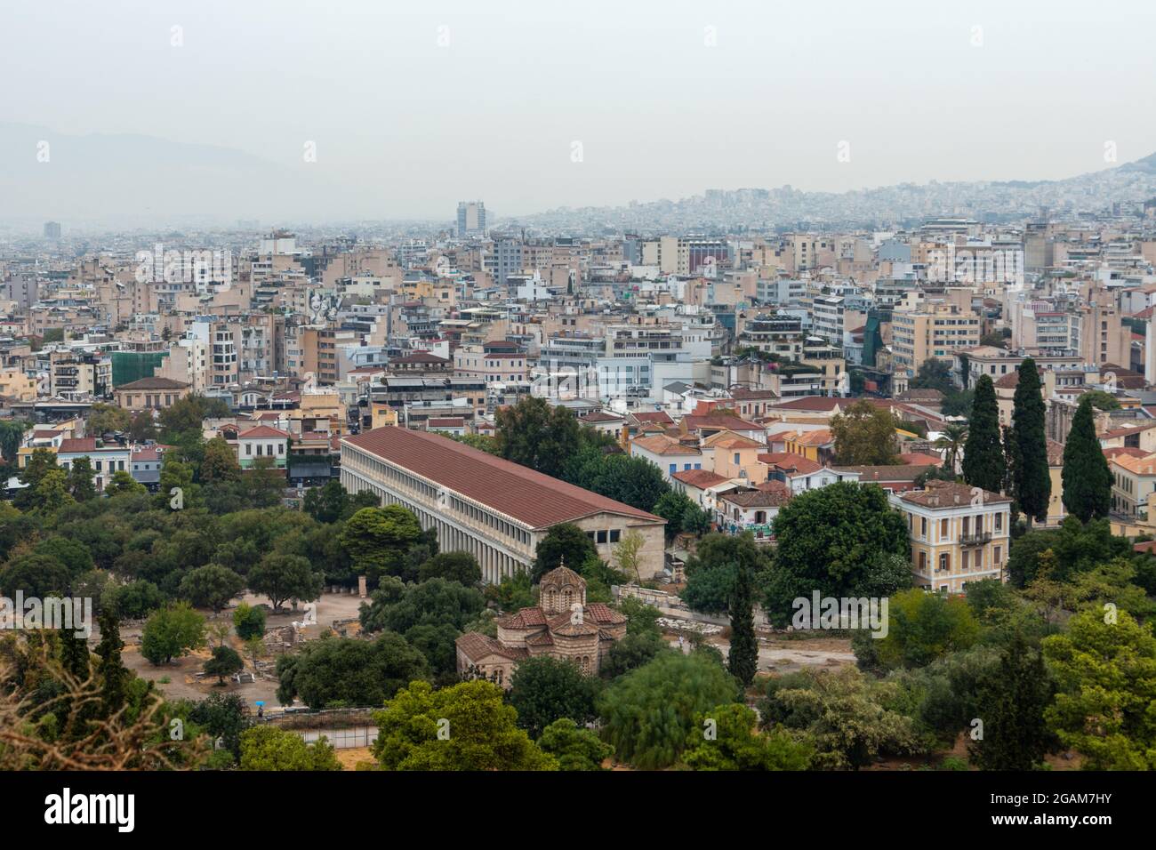 Stoa of Attalos in greenery, Church of the Holy Apostles and Athens city center with rocky hill in gray foggy day from Areopagus - Hill near Acropolis Stock Photo