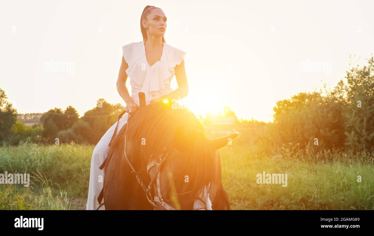 Professional model rides large stallion along meadow Stock Photo - Alamy
