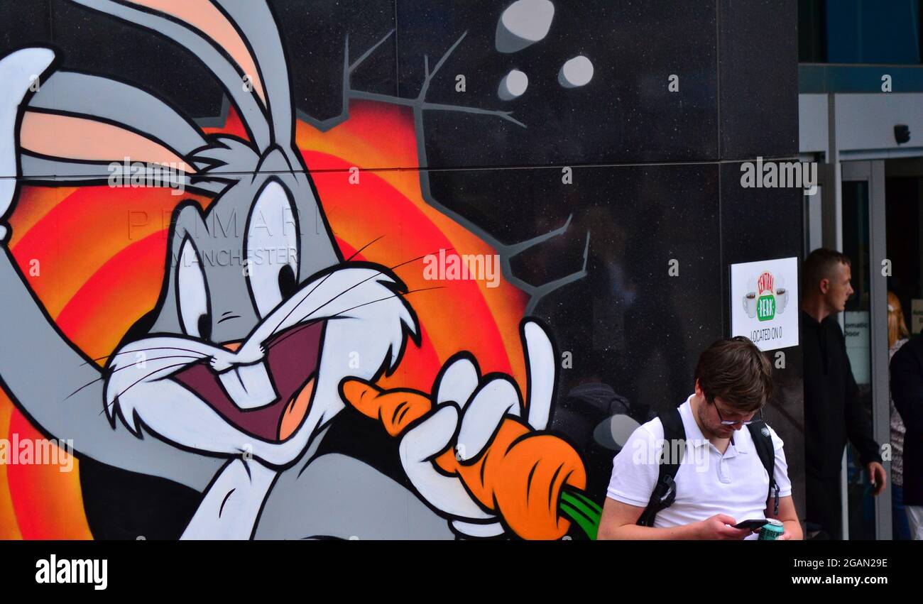 A man checks his phone next to a cartoon image of Bugs Bunny on the side of the Primark store in city centre Manchester, England, United Kingdom, Stock Photo