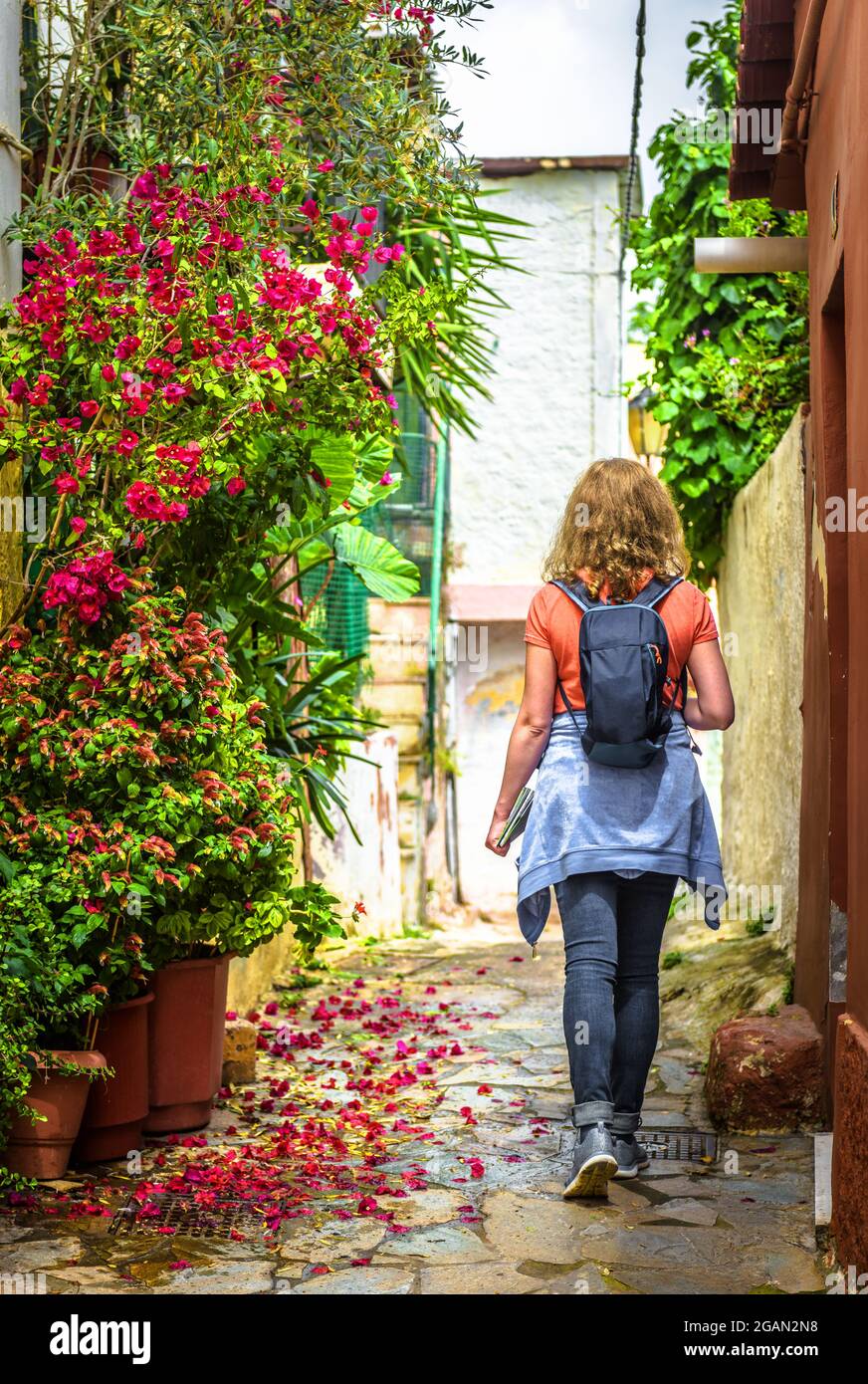 Street in Plaka district, Athens, Greece, Europe. Scenic alley with plants and flowers in Athens city center. Girl tourist walks on nice landscaped si Stock Photo