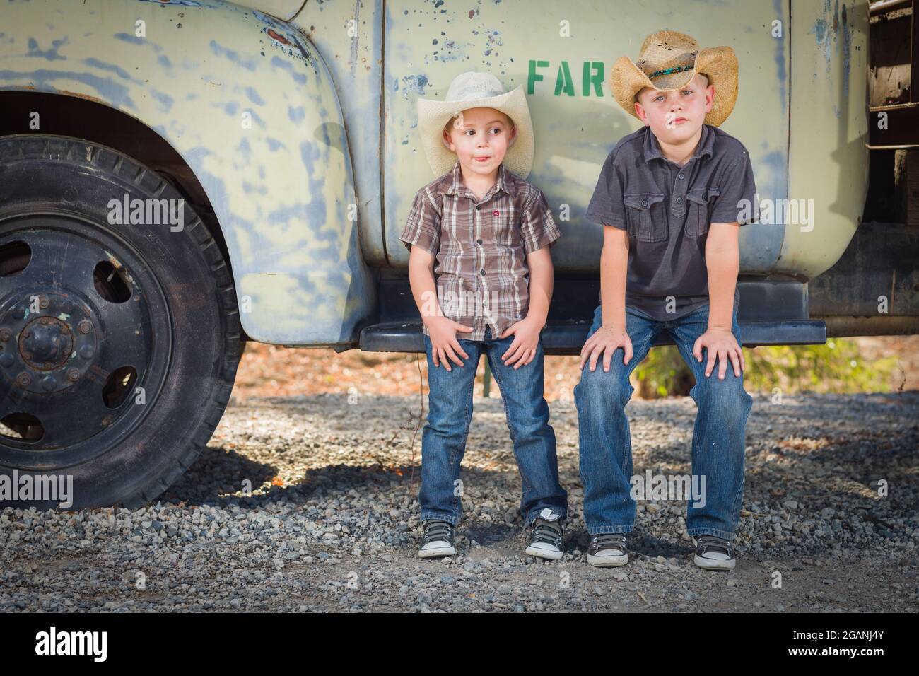 Two Young Boys Wearing Cowboy Hats Leaning Against an Antique Truck in
