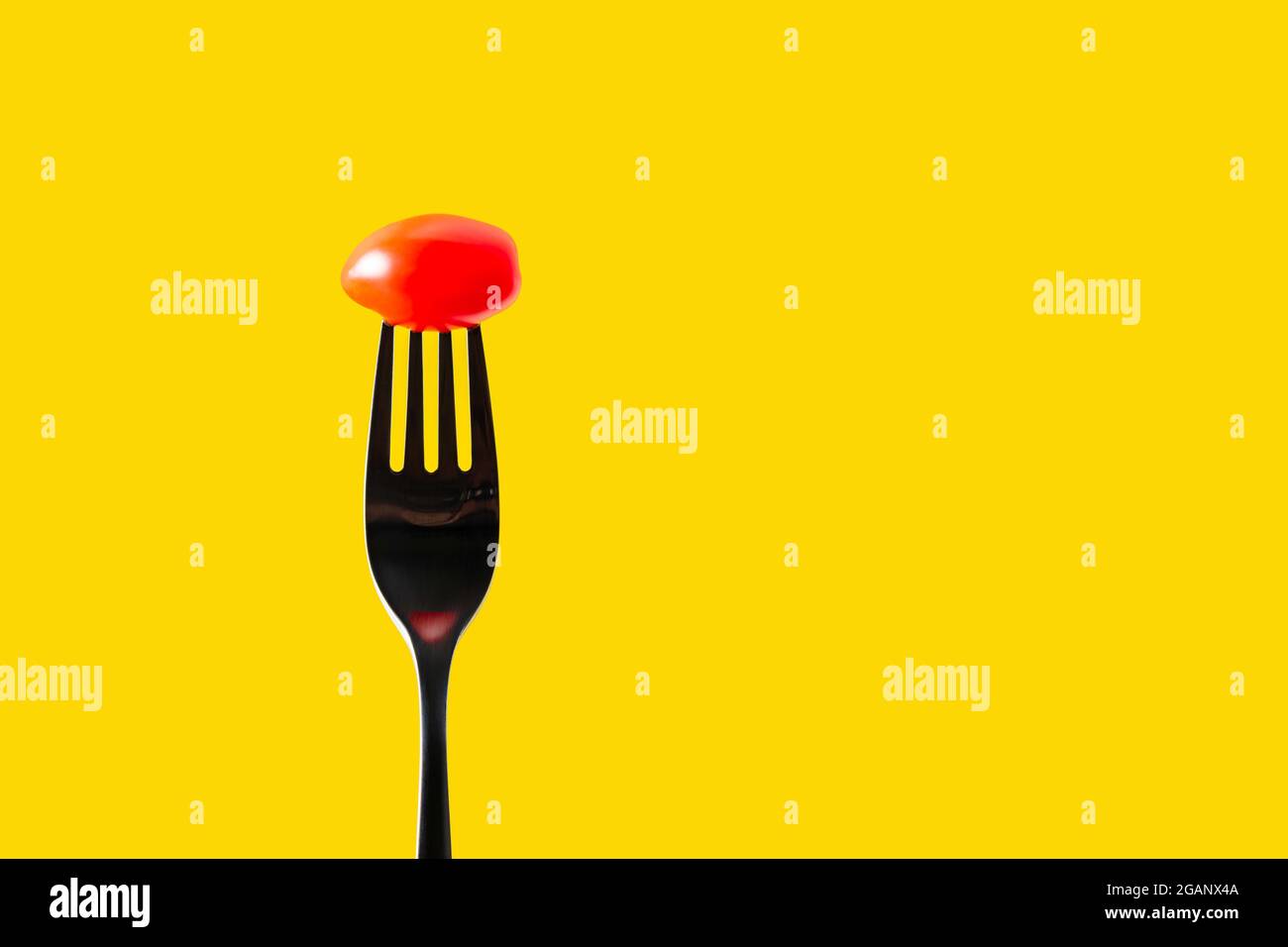 Fork with tomato on yellow background, copy space for text  Stock Photo