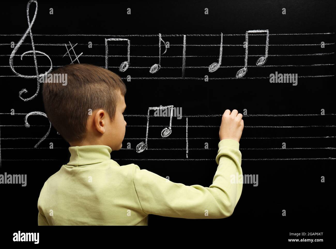 Boy Opening Note Cute boy writing at the blackboard with musical notes, in the classroom ...